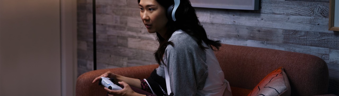  一位女性頭戴著耳機(jī)，手持Playstation手柄，沉浸在她的娛樂世界中。