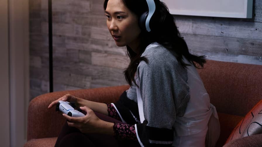  一位女性頭戴著耳機(jī)，手持Playstation手柄，沉浸在她的娛樂世界中。